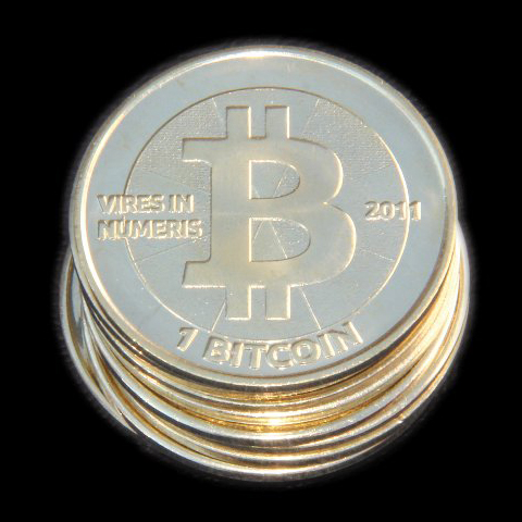 A 2012 Casascius 1 BTC coin. The hologram conceals a private key; the rim carries the motto VIRES IN NUMERIS.